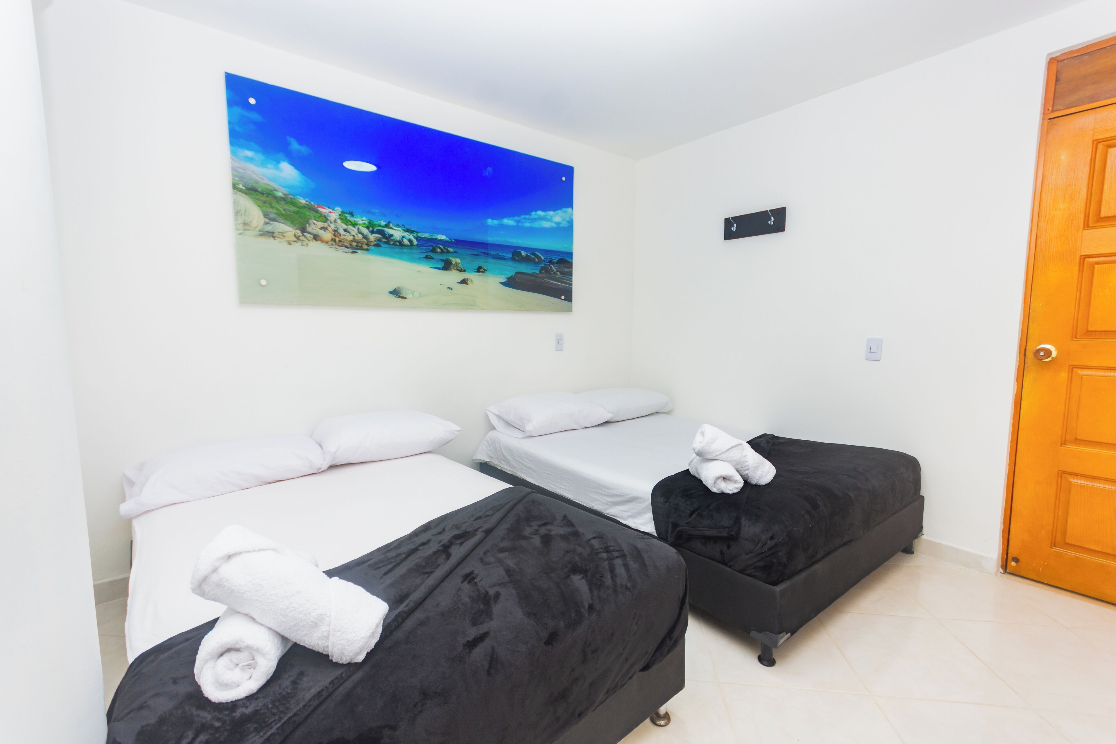 A hotel room with two beds, a painting of a beach scene, and a wooden door.