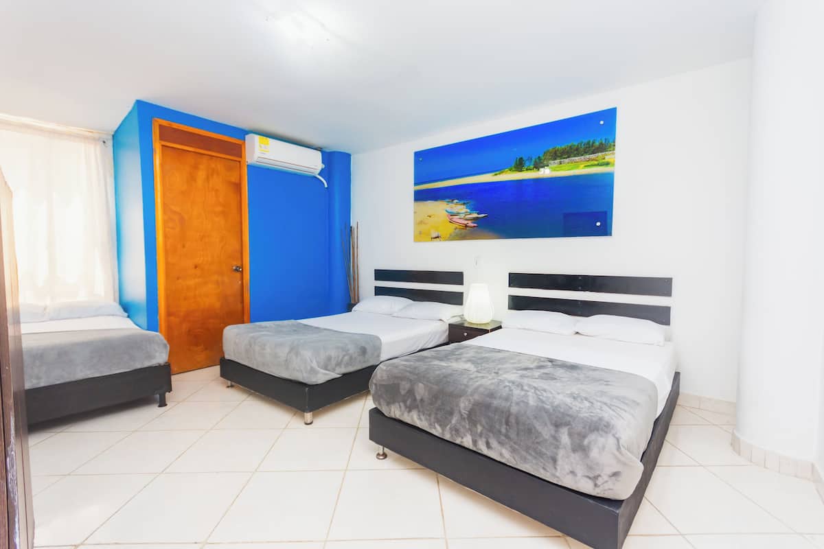 A hotel room with three beds, a wooden door, and a beach scene painting on the wall.