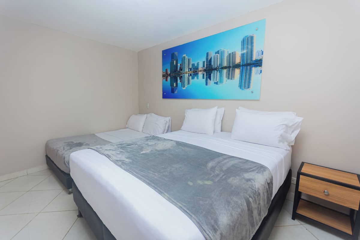 A hotel room with a large bed, a nightstand, and a cityscape painting on the wall.