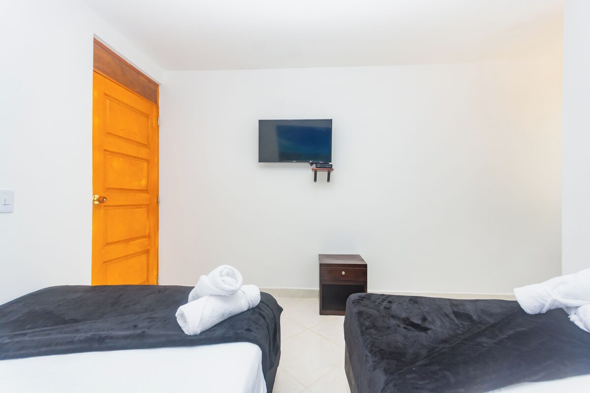 Ein Hotelzimmer mit zwei Betten, einem Fernseher an der Wand und einer Holztür.