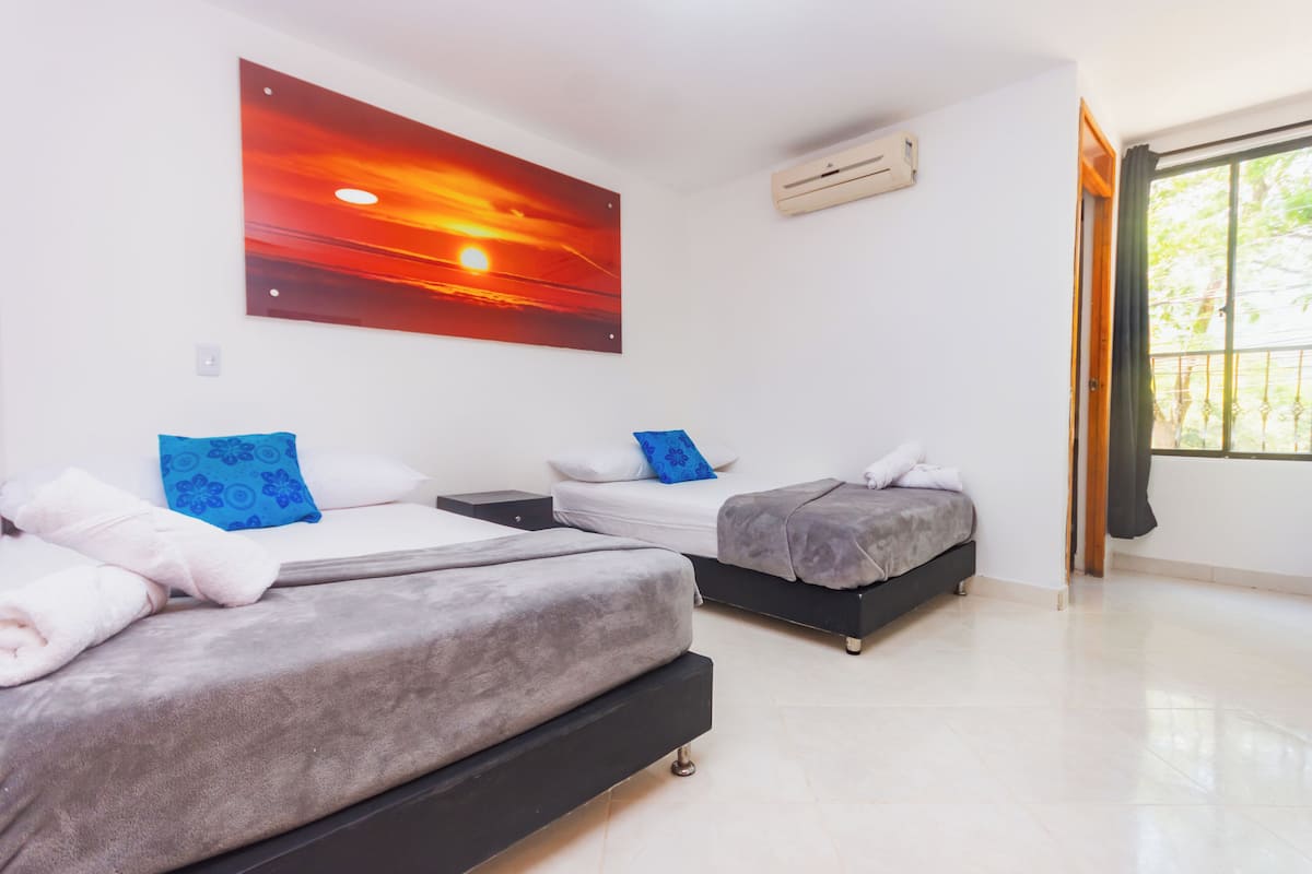 A bedroom with two beds, a large painting of a sunset, and an air conditioning unit.