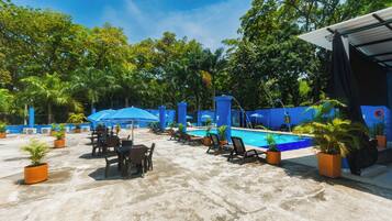 Un área de piscina en la azotea con sillones de descanso y sombrillas, rodeada de plantas en macetas y árboles.