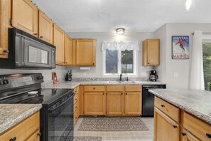 A kitchen with wooden cabinets, a stove, a dishwasher, and a window with a view. - Eden Ridge Townhouse 5-C (Bethel)