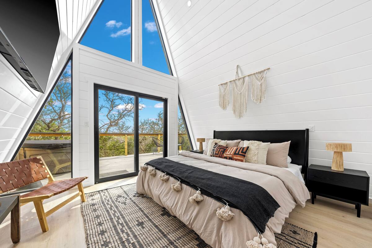 A bedroom with a large bed, a bench, a nightstand, and a macrame wall hanging.