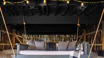 Un lit-balançoire rustique en bois, doté d’un matelas, de coussins et d’une couverture, et suspendu par des cordes.