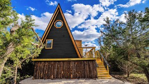 Una cabaña con techo triangular, terraza de madera y una ventana pequeña.