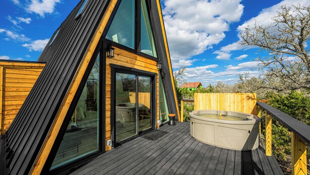 Una estructura moderna tipo cabaña con grandes ventanales, una terraza de madera y un jacuzzi.