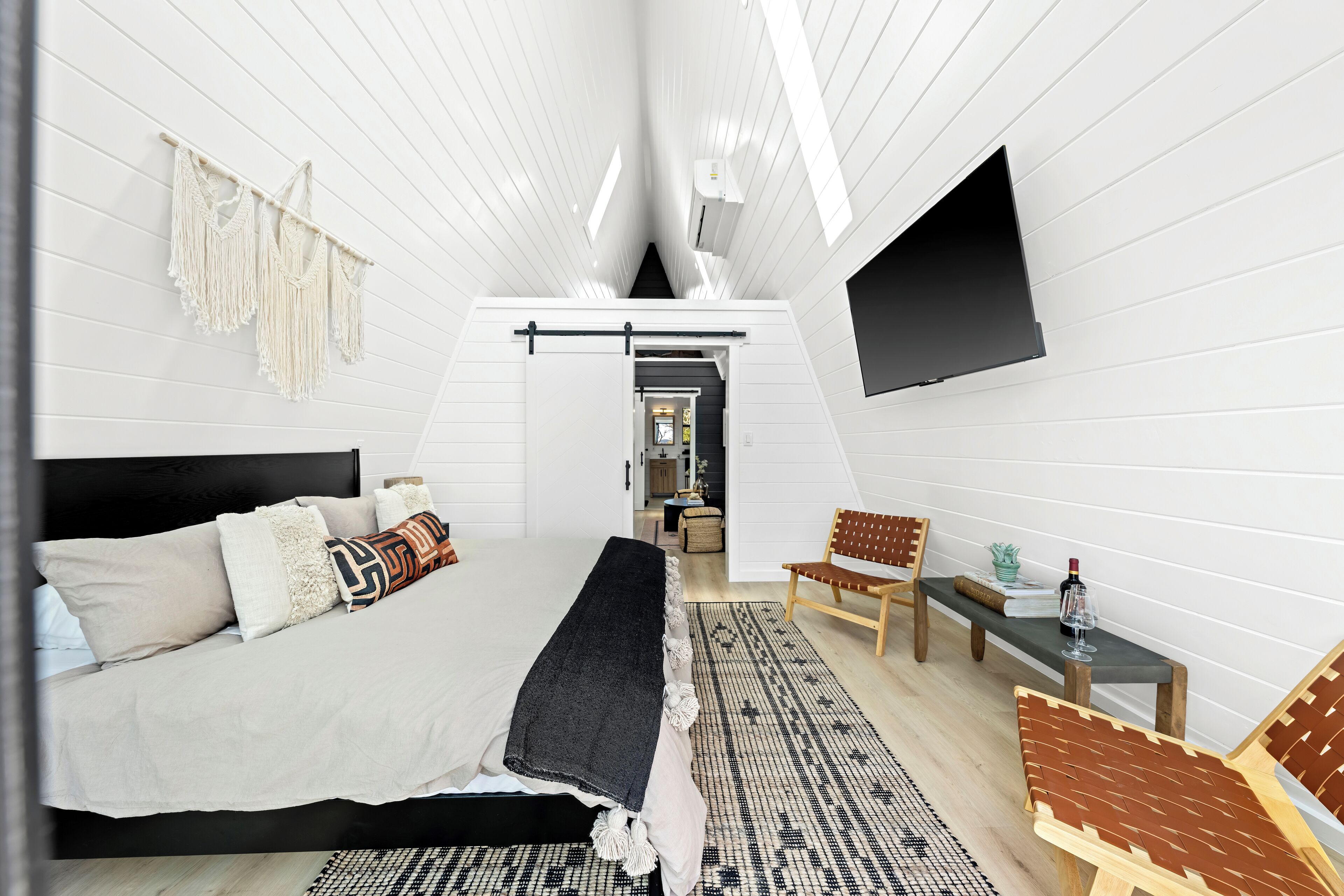 A modern bedroom with a bed, a TV, a bench, and a small table with a bottle.