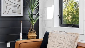 Una habitación con una pared de madera oscura, una obra de arte abstracta enmarcada, una planta en maceta, una vela y una ventana con vistas a árboles.