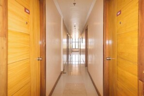 A hotel corridor with wooden doors, a tiled floor, and a ceiling with recessed lighting. - RedDoorz @ Benelio Suites Pavia Iloilo (Pavia)