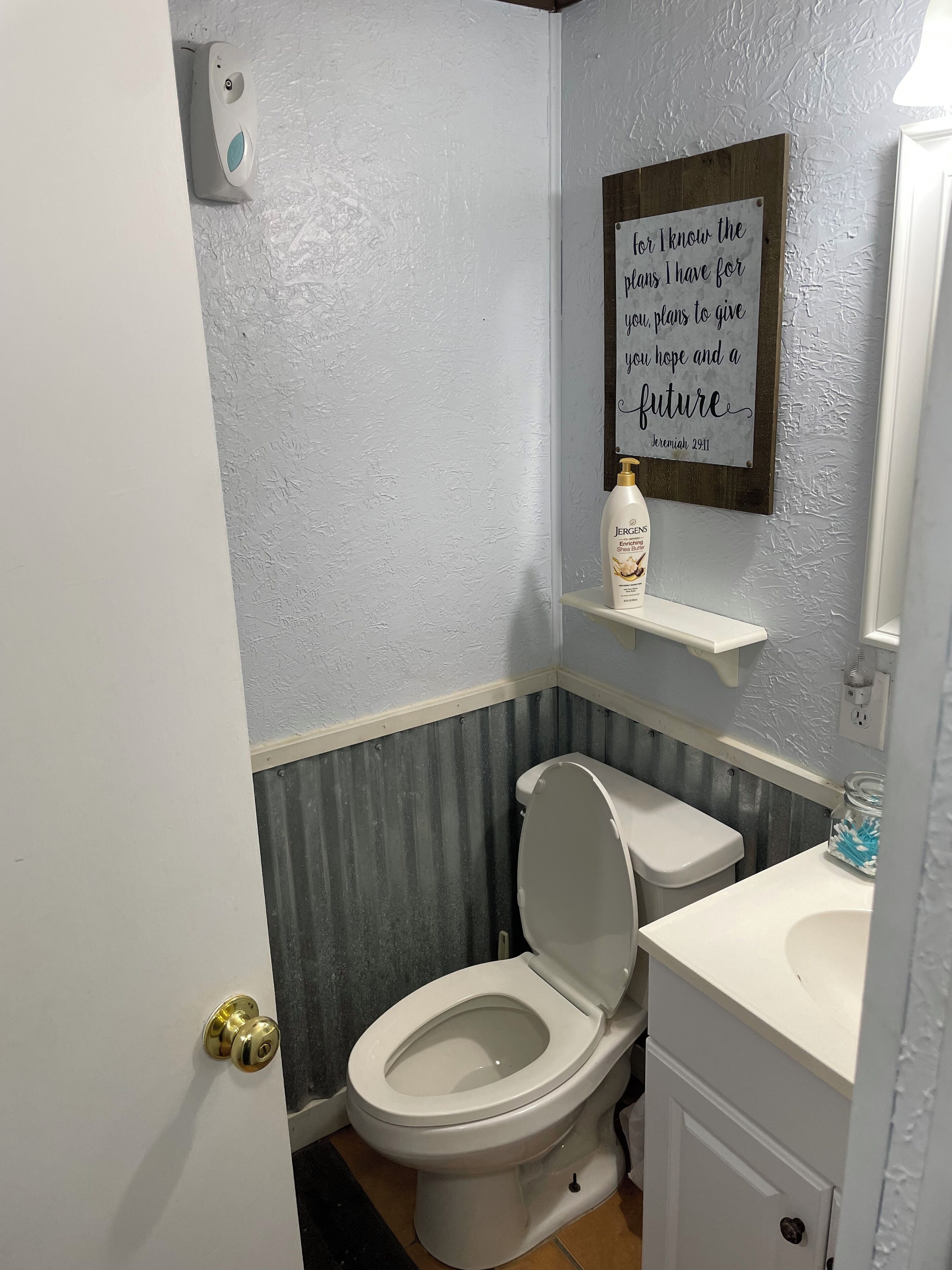 A bathroom with a toilet, a shelf with a bottle, and a motivational quote on the wall.