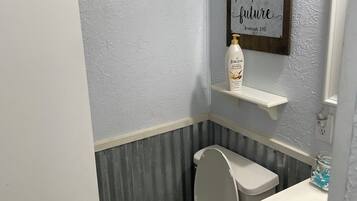 A bathroom with a toilet, a shelf with a bottle, and a motivational quote on the wall.