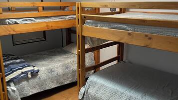 A dormitory room with bunk beds, a window with blinds, and a ceiling light.