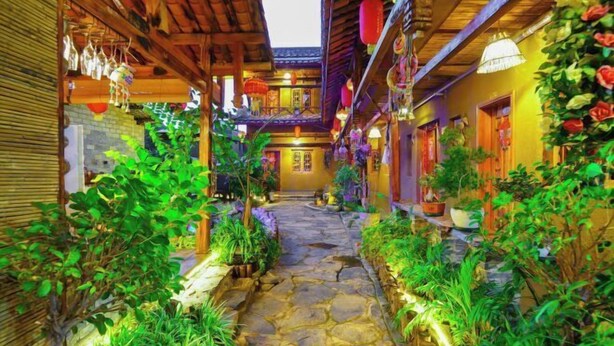 Un étroit sentier de pierre, bordé d’une végétation luxuriante et de bâtiments en bois à l’architecture traditionnelle.