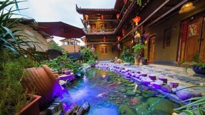 Une cour traditionnelle agrémentée d’un élément d’eau, de plantes en pot et d’un immeuble à plusieurs étages doté de balcons.