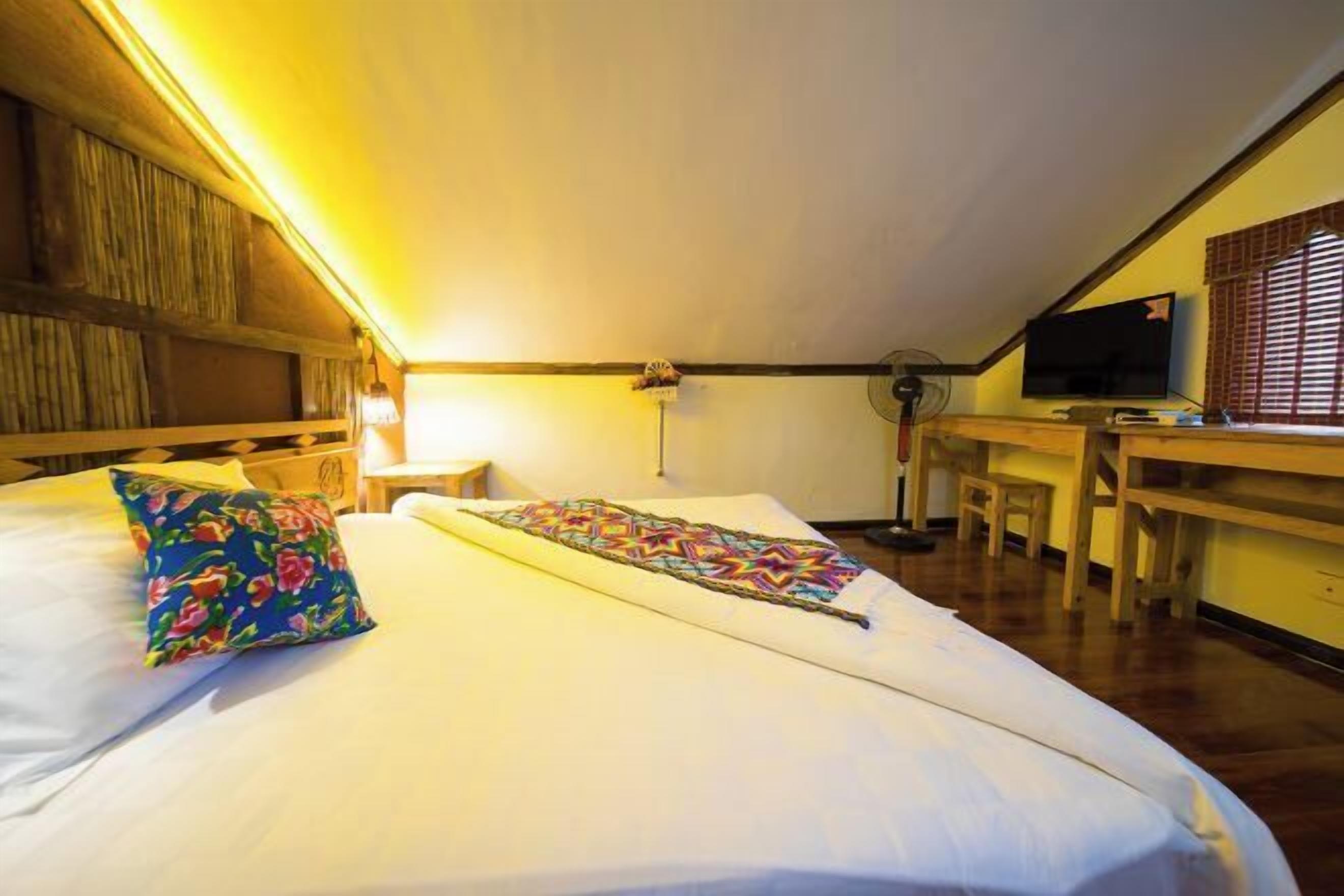 Una habitación con cama, escritorio, silla, televisión y ventilador.