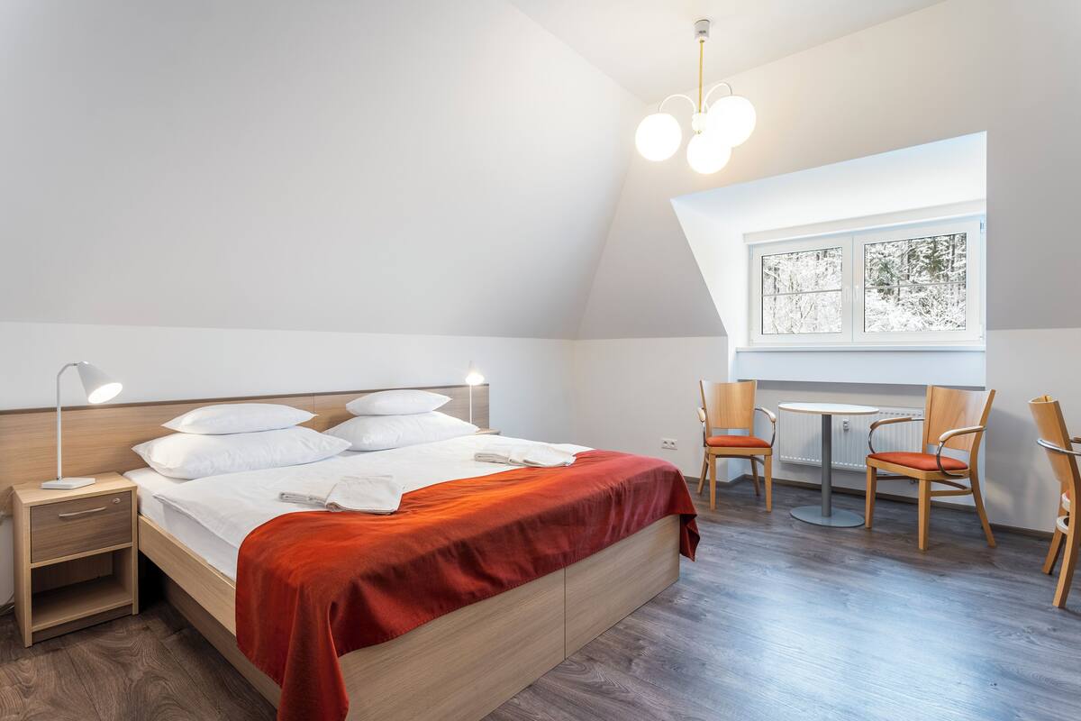Une chambre à coucher comprenant un lit, une table de chevet, une lampe et une fenêtre donnant sur des arbres.