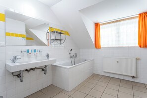 Un baño moderno con dos lavamanos, una bañera y un ventanal con cortinas naranjas.