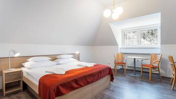 A bedroom with a bed, bedside table, lamp, and a window with a view of trees.