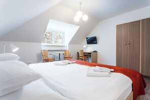 Habitación de hotel con una cama grande, un escritorio, dos sillas, un televisor y un armario.