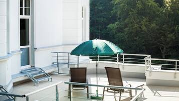 Ein Balkon mit einem grünen Sonnenschirm, zwei Korbstühlen und einem Glastisch.
