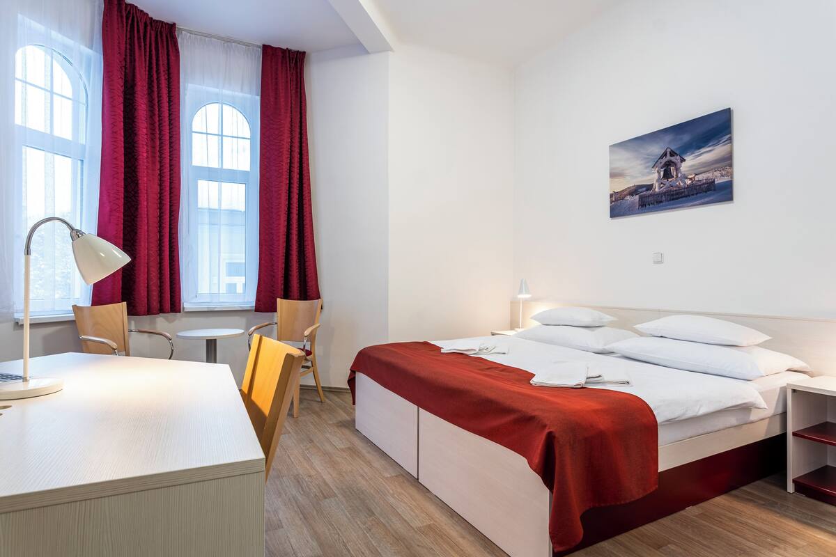 Une chambre d’hôtel avec un lit, un bureau, une chaise, une petite table et un tableau au mur.