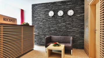 A reception area with a stone wall, three clocks, a reception desk, a brown sofa, and a small table with a flower arrangement.