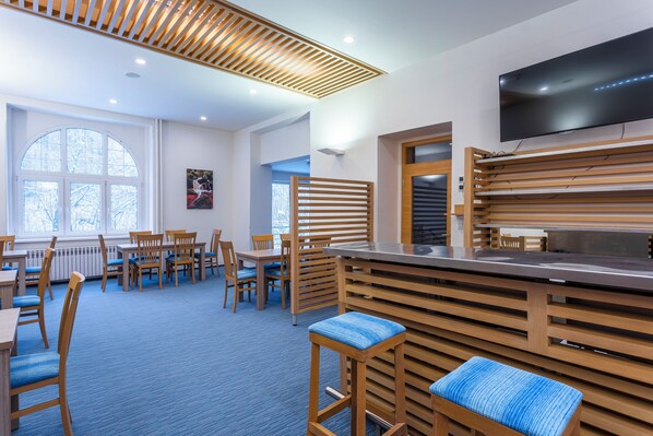 A modern restaurant with wooden furniture, a flat-screen TV, and large windows. - Apartmánový Komplex Dagmar (Jachymov)