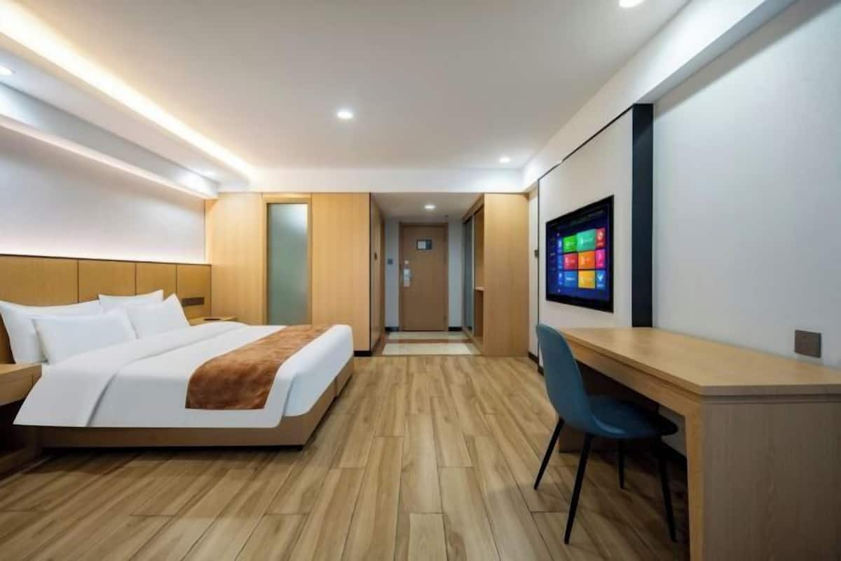 A modern hotel room with a bed, a desk, and a TV on the wall.