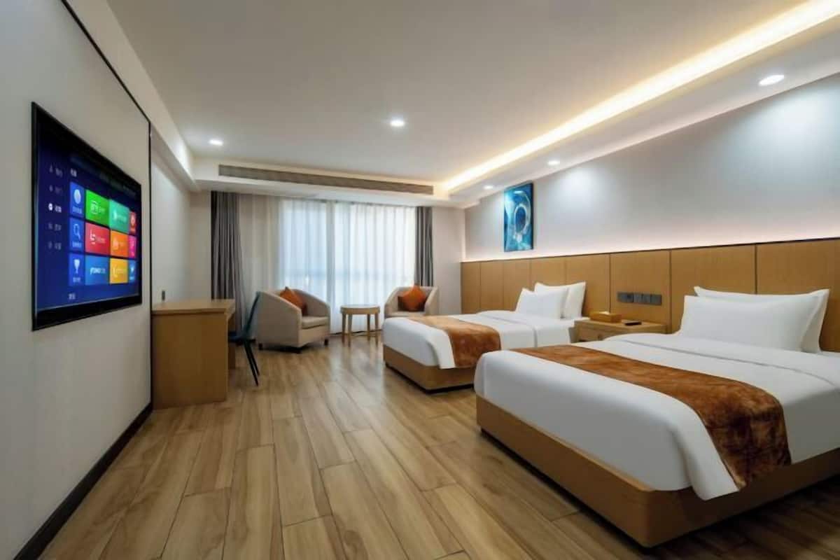A hotel room with two beds, a TV mounted on the wall, a desk, and a chair.