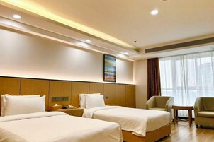 Habitación de hotel con dos camas, cabecero de madera, un cuadro en la pared, una ventana con cortinas y una mesita.