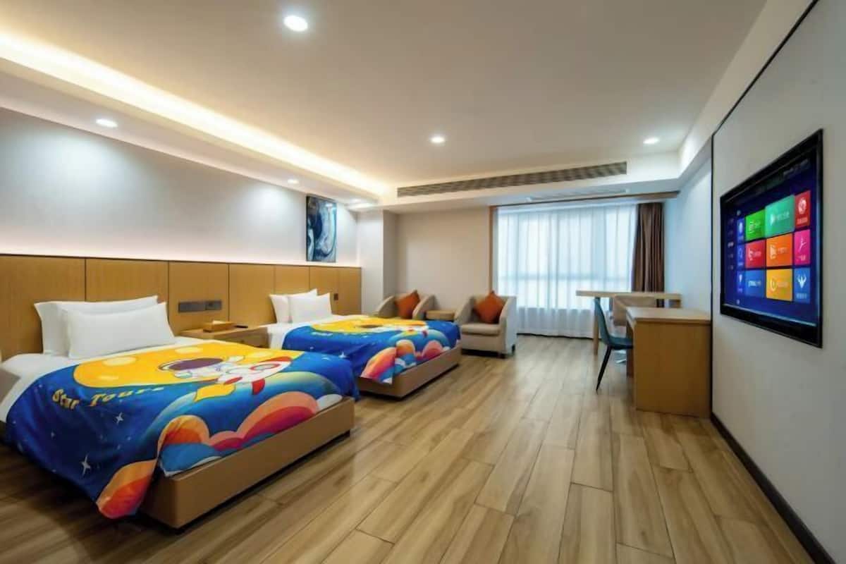 A hotel room with two beds, a TV, a desk, and a window with curtains.