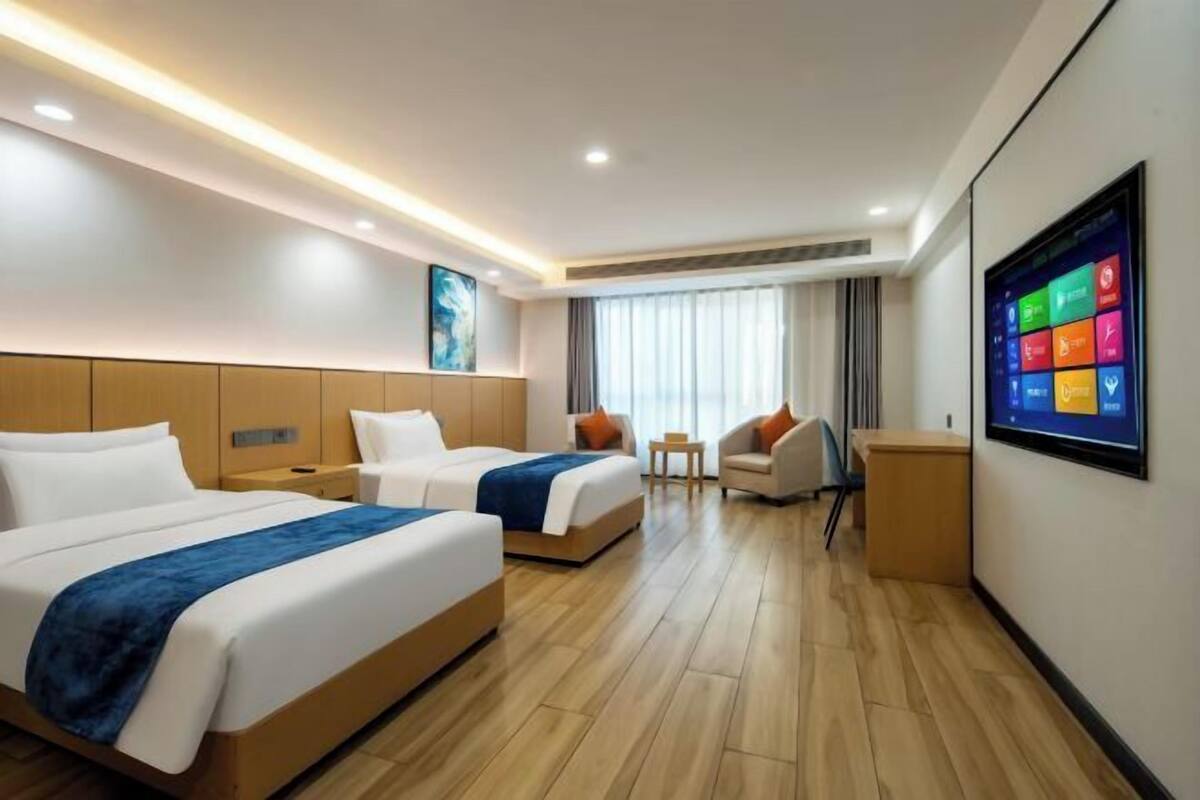A hotel room with two beds, a TV, a desk, and a chair.