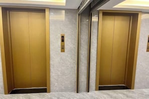 Two elevator doors with a gold finish and a control panel between them.