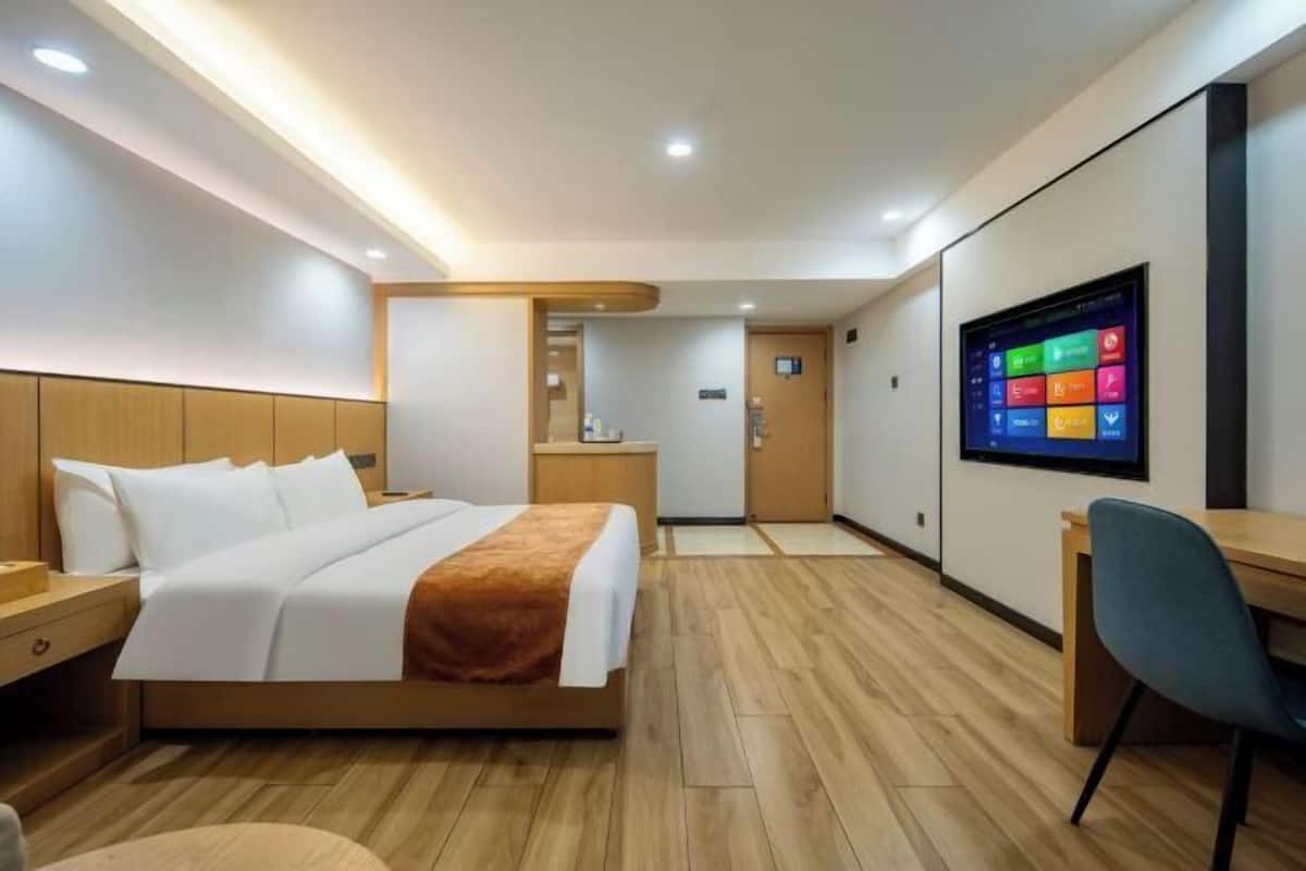 A modern hotel room with a bed, desk, chair, and a TV displaying colorful icons.