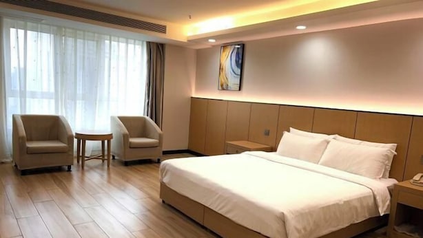 A hotel room with a large bed, two armchairs, a small table, and a bedside table with a lamp. - Wanbang Zundi Hotel (Xi'an High-tech Wanda Plaza Mutasi Subway Station Branch) (Xi'an)