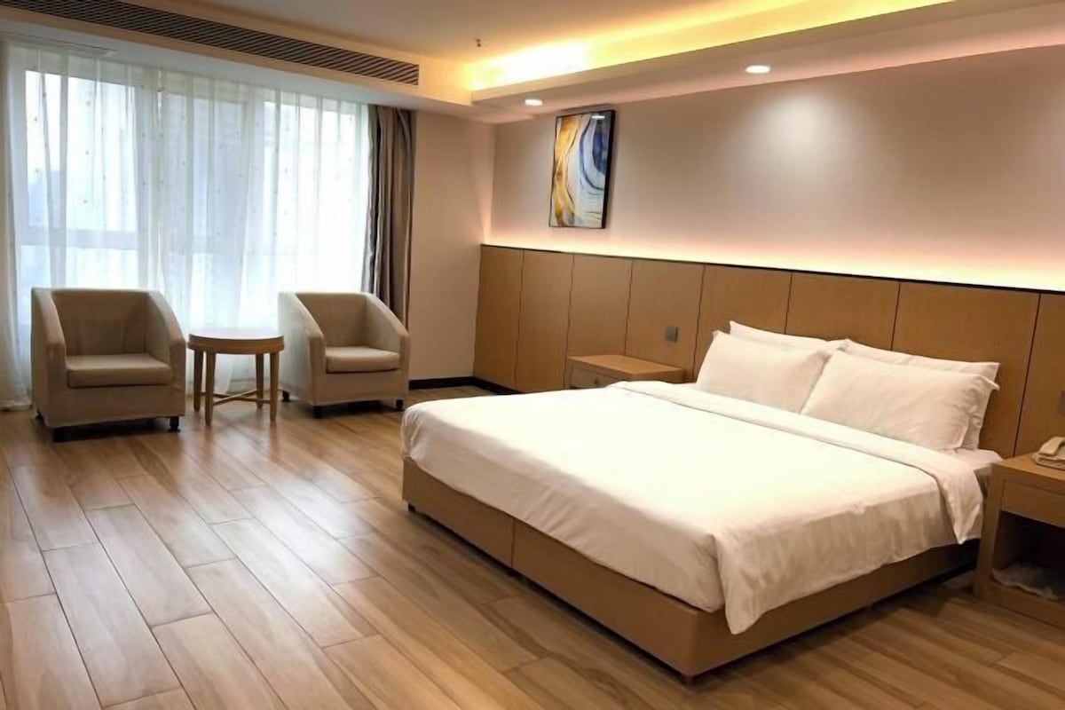 A hotel room with a large bed, two armchairs, a small table, and a bedside table with a lamp.