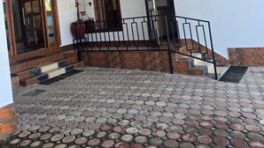 Una entrada de edificio con un patio empedrado, escalones de madera y una barandilla metálica.
