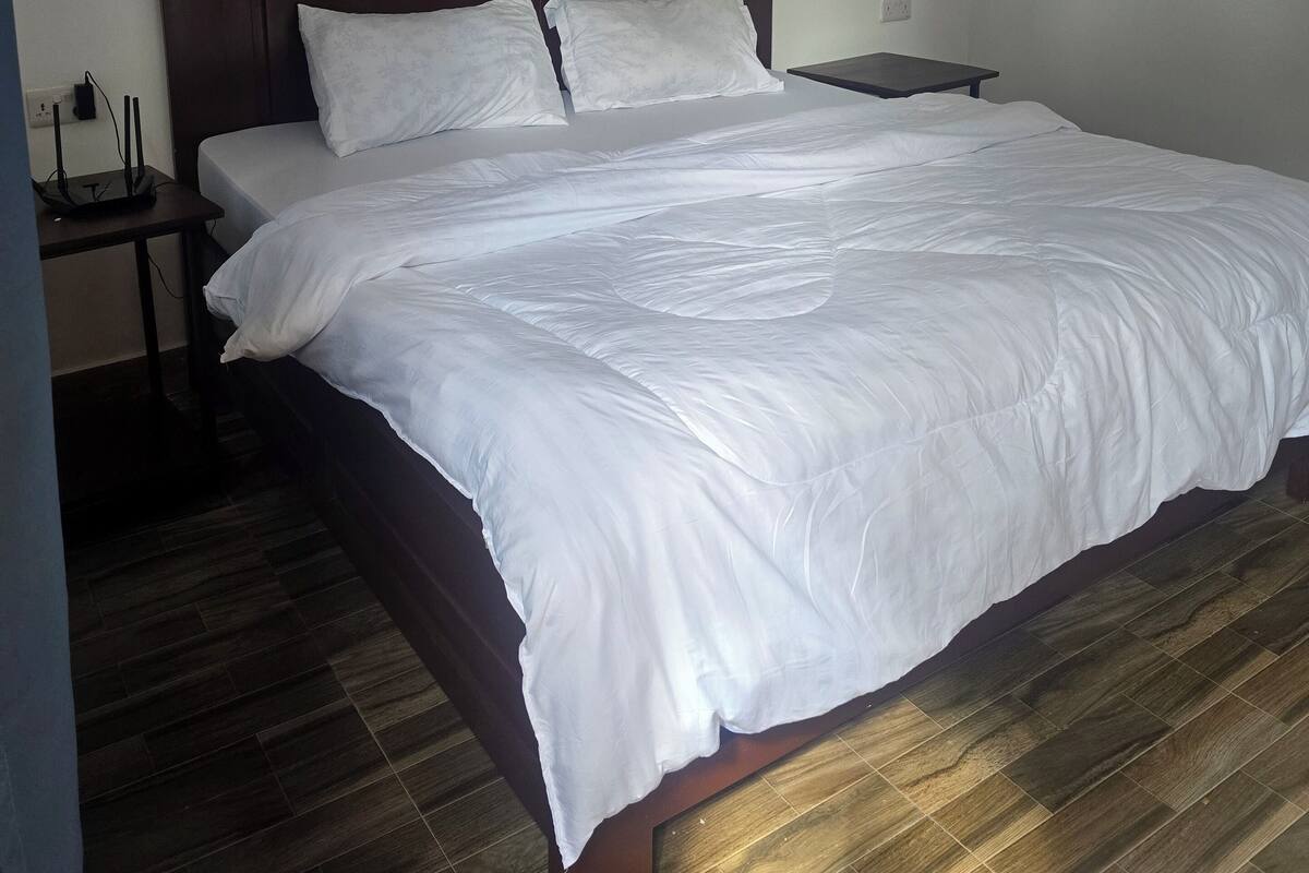 A neatly made bed with white linens in a room with a wooden floor and a simple headboard.