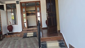 Un recibidor amplio con suelo de baldosas, una escalera de madera y una puerta grande con reja de metal.