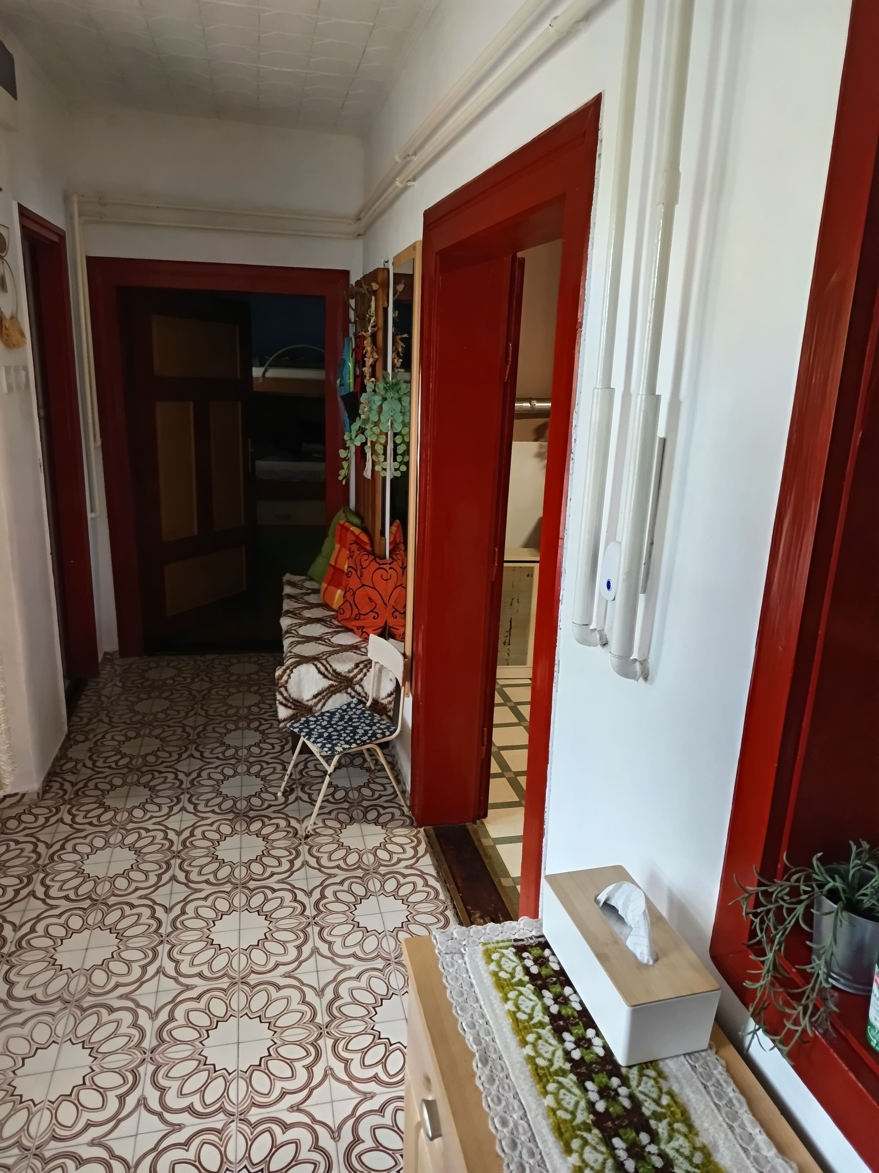 A hallway with patterned flooring, a chair, a tissue box, and a plant.