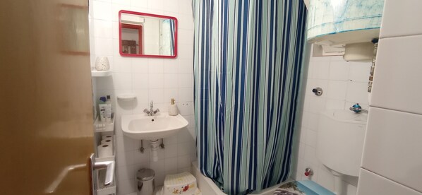 Un baño con lavamanos blanco, un espejo, cortina de ducha a rayas y un inodoro.