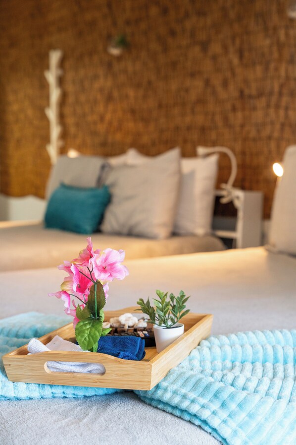 A neatly made bed with a blue towel, a wooden tray with a potted plant, and a pink flower arrangement.