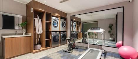 A modern laundry room with a treadmill, exercise balls, and a large mirror.