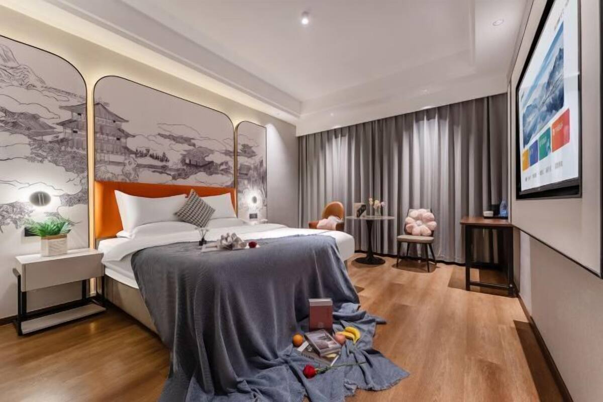 A modern bedroom with a bed, bedside table, nightstand, and a large wall-mounted artwork.