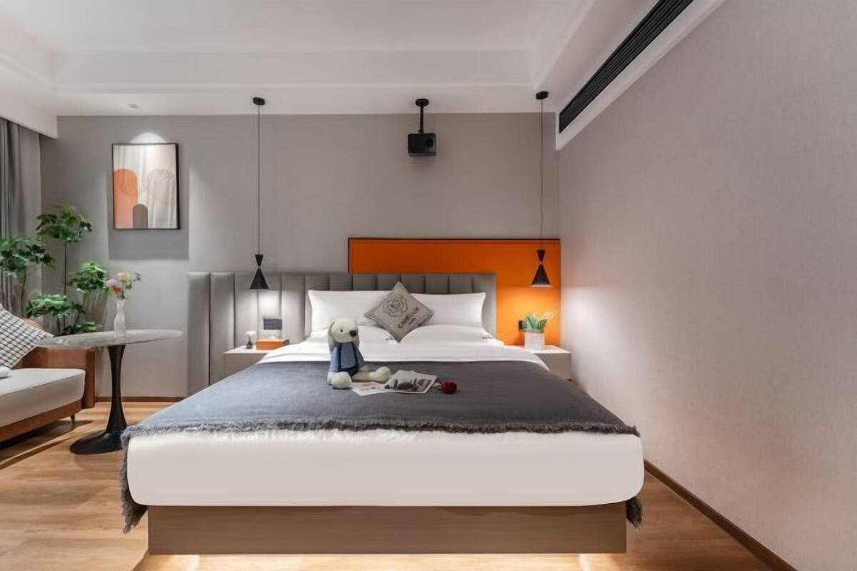 A modern bedroom with a bed, bedside tables, a nightstand, a lamp, and a wall-mounted projector.