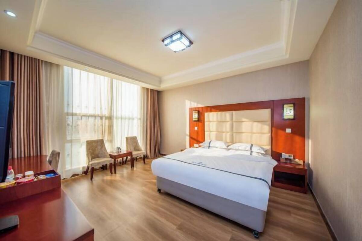 A hotel room with a large bed, a desk with a chair, a TV, and a window with curtains.