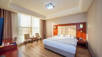 A hotel room with a large bed, a desk with a chair, a TV, and a window with curtains.