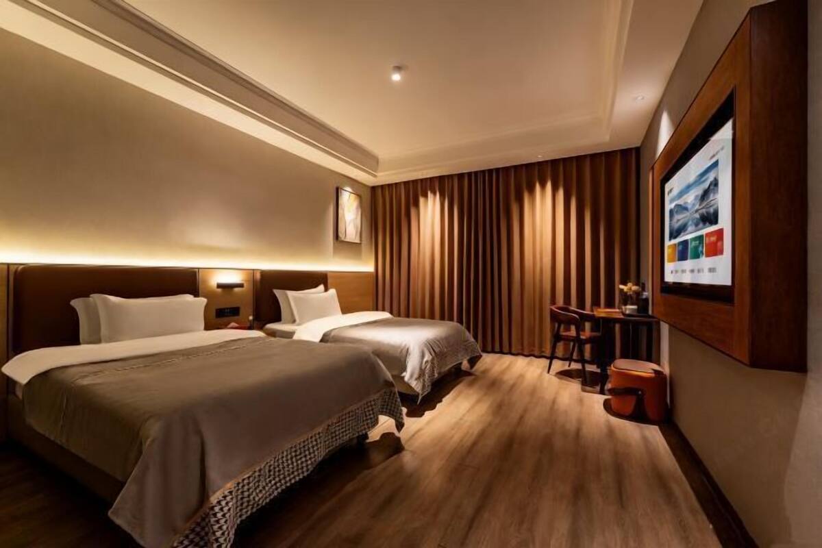 A hotel room with two beds, a desk, a chair, and a large poster on the wall.