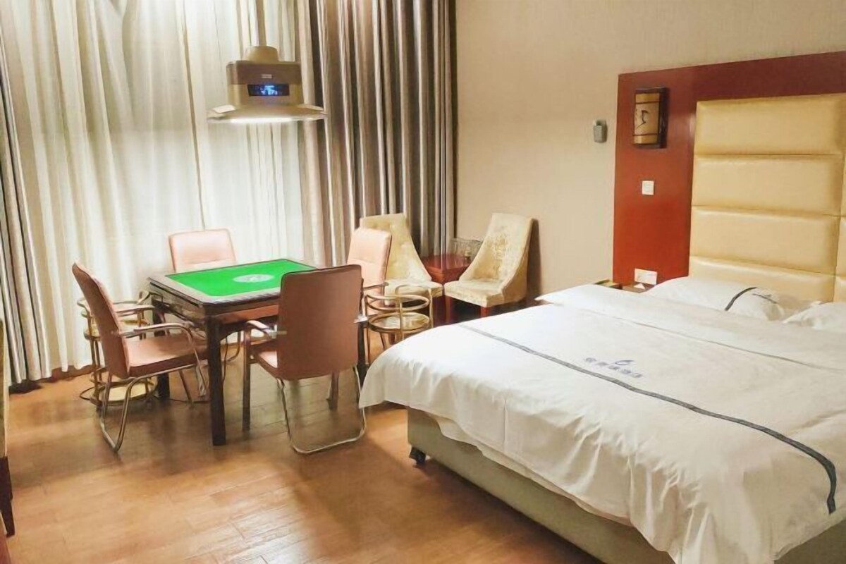 A hotel room with a bed, a desk with a green table, and two chairs.